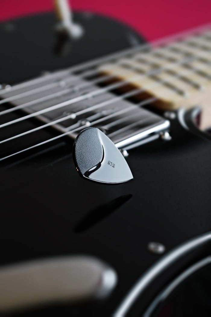 Close-up of a black electric guitar with a metal pick highlighting the strings and glossy finish.