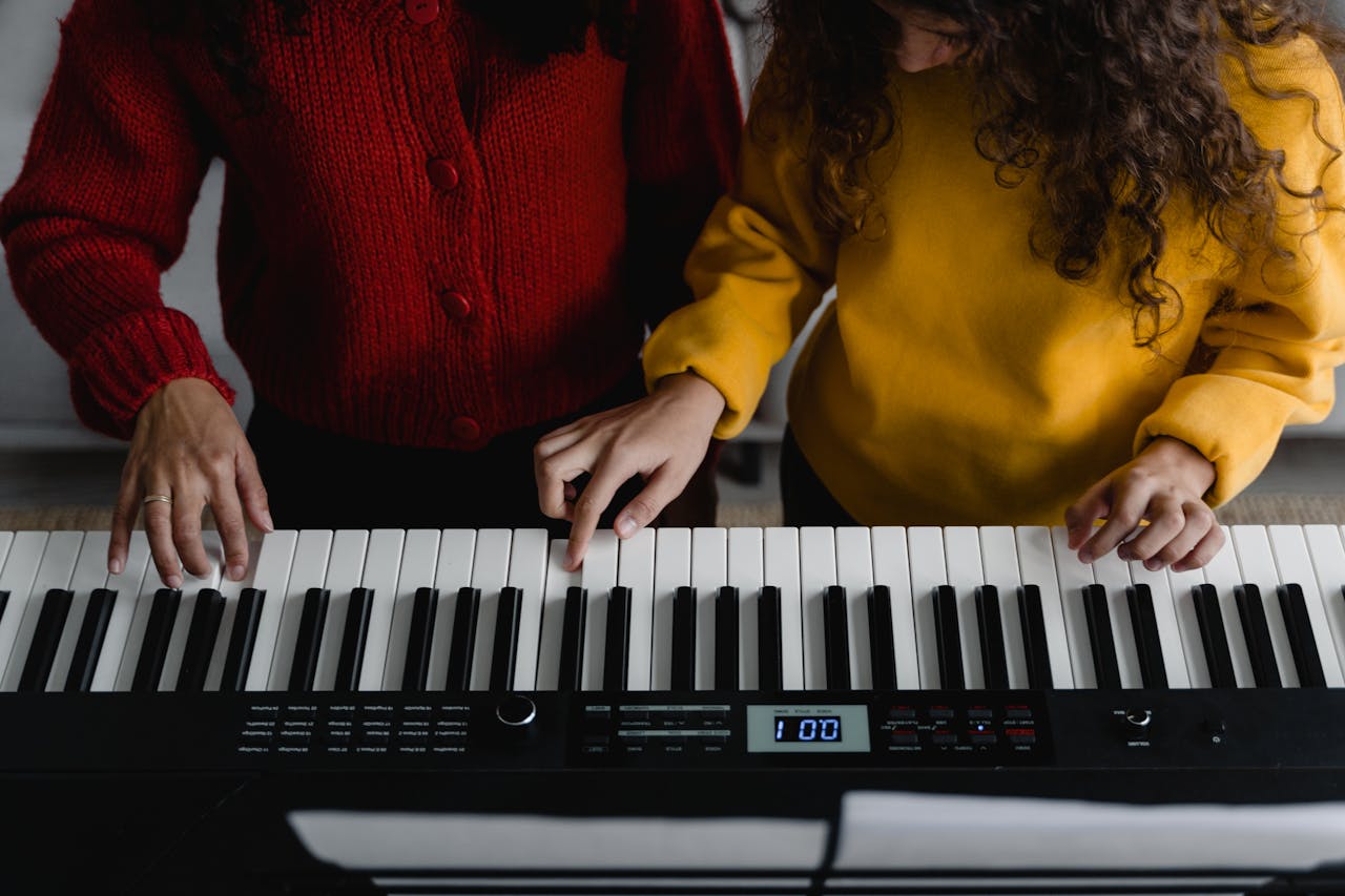 about-us Two women playing electronic keyboard indoors. Focus on hands and instrument keys.